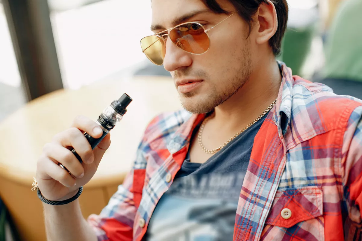 Stylish man in sunglasses holds black vape pen, symbolizing modern smoking alternatives.
