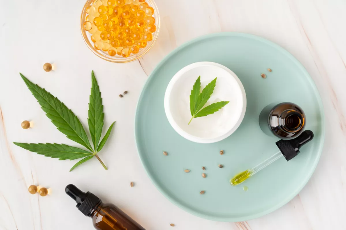 Cannabis leaf, CBD oil dropper, cream, and hemp capsules on wooden surface for wellness.