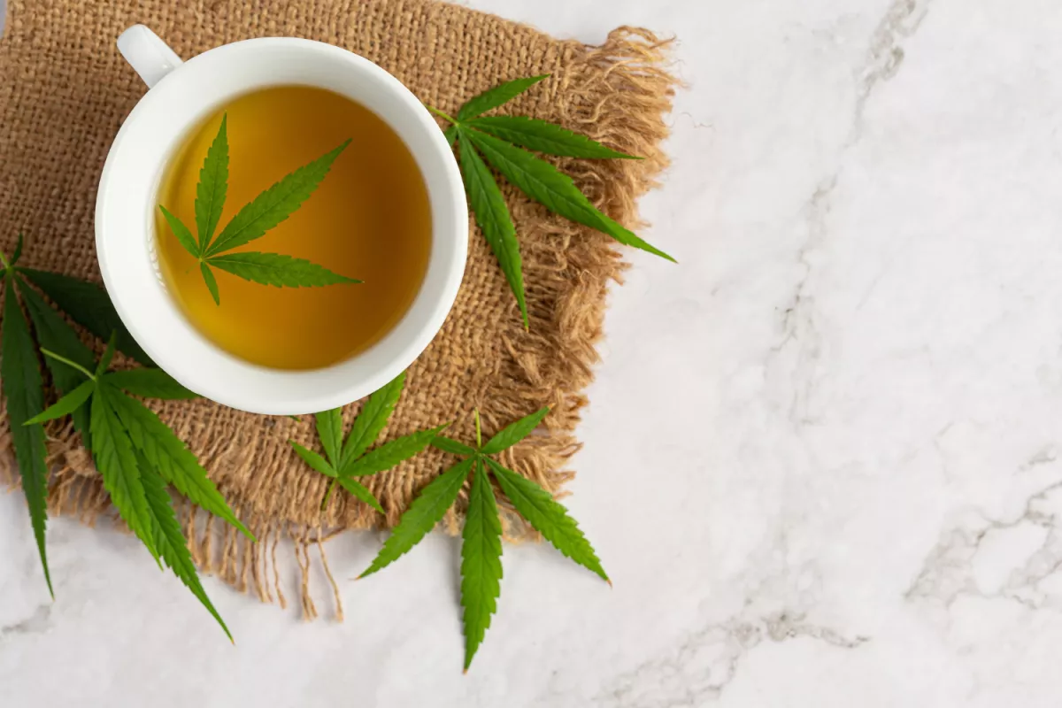 CBD-infused cannabis tea in a white cup on marble, with fresh leaves for natural wellness.